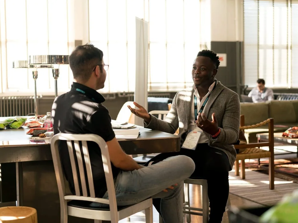 Two people talking across a table in a sunlit office